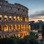 The Colosseum lit from within at dusk, seen through trees